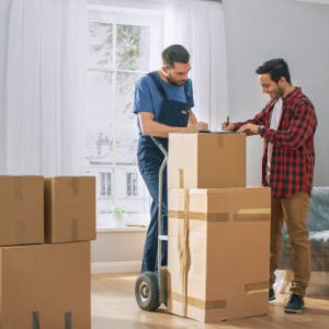 Happy New Homeowner Welcomes Professional Mover with Hand Truck full of Cardboard Boxes, Receives His Goods and Signs on Clipboard.